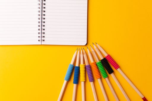 A top view of an open journal and pencils isolated on a yellow background