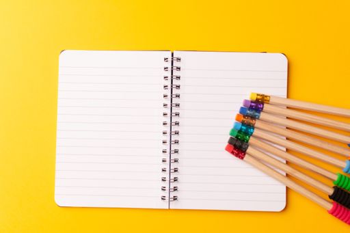 A top view of an open journal and pencils with colorful rubbers isolated on a yellow background