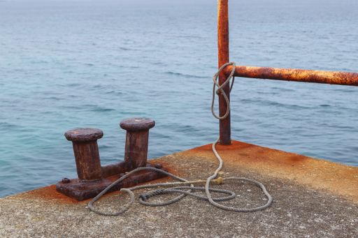 A selective focus shot of a mooring bollard, ropes, and railing