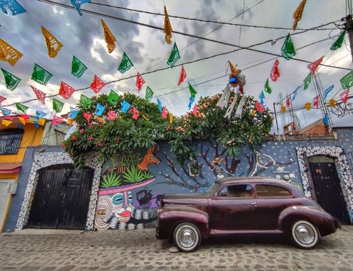 An old car is parked in front of a brightly-painted wall in a Mexican city