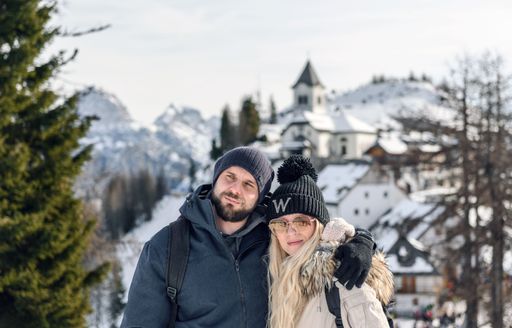 The couple in front of mountaintop village of Monte Lussari in Julian alps, Italy