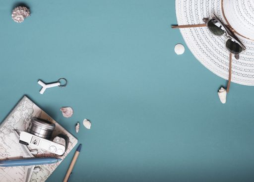 A concept shot conveying summer vacation with a summer hat, sunglasses, seashells camera and toy plane on teal background