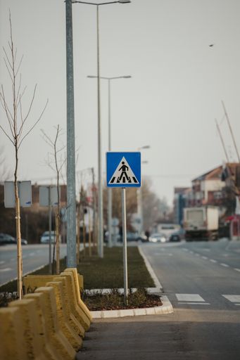 A vertical shot of a road sign of a pedestrian walkway with white traffic marking.