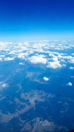 A vertical shot of a bright sky with white clouds from an airplane window