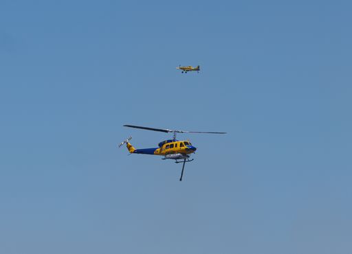 A helicopter water fire bomber, with a water bomber plane in the background