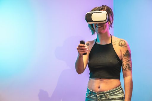 A portrait of a young happy Spanish woman with tattoos playing games on VR glasses