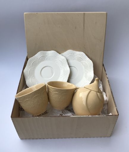 A closeup of a brown and white ceramic tea set in a box against a gray background