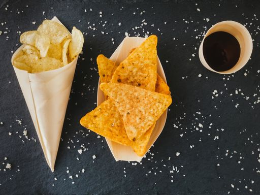 A top view of crunchy salted triangle-shaped corn chips and potatoe chips served in paper on a table
