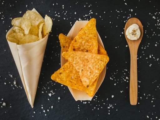 A top view of crunchy salted triangle-shaped corn chips and potatoe chips served in paper with sauce