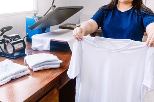 A female holding a white T-shirt next to the cloths printing machine and T-shirts on the wooden table