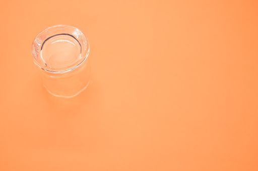 A high angle shot of a small shot glass on an orange background under the lights