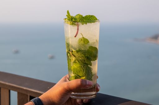 A woman holding a cup of refreshing cold mojito cocktail with mint leaves in a rooftop bar in Thailand
