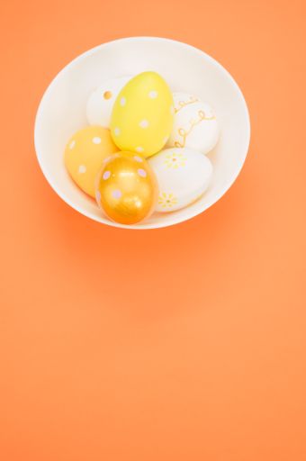 A vertical shot of a bowl with Easter egg decorations on an orange surface
