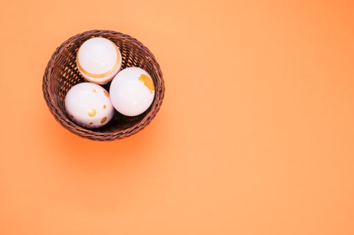 A top view of a basket of decorated eggs for Easter on an orange surface
