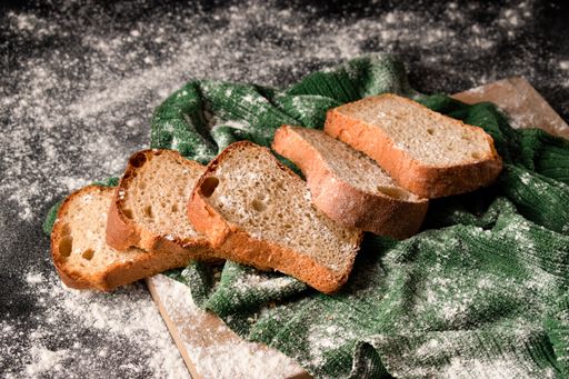 Fresh homemade sliced loaf of bread on fabric textile with spilled flour on a dark rustic table surface