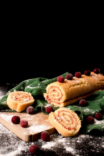 An appetizing homemade biscuit roll decorated with fresh berries on fabric textile with spilled flour