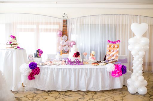 A birthday table decorated with pink and white balloons and donuts