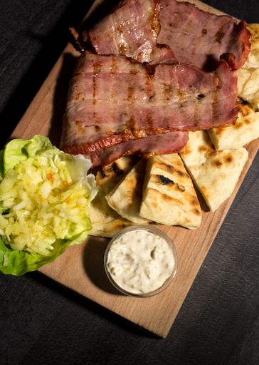 A vertical high angle of grilled meat on bread served with salad and sauce on a wooden plate