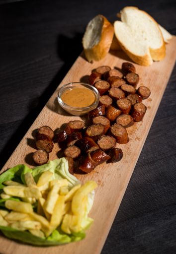 A vertical closeup of sliced sausage and bread served with fries and sauce on a wooden plate