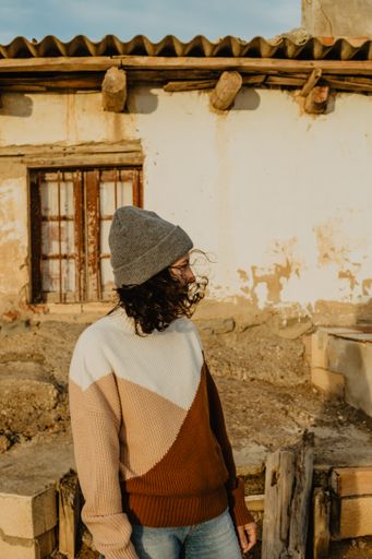 A woman wearing a warm sweater and a beanie cap standing near an old house in a village