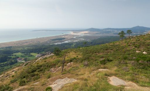 A landscape of the Dunas de Corrubedo park covered in greenery surrounded by the sea in SPa