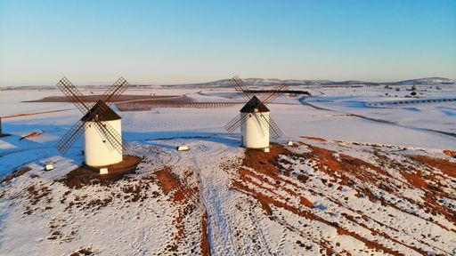 An aerial shot of windmills in a snow-covered area under the clear sky