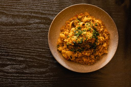 A bowl of delicious rice with cuttlefish and prawns on a wooden table