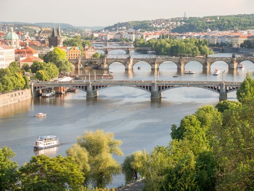 A landscape of the Vltava River with bridges over it surrounded by greenery and buildings in Prague