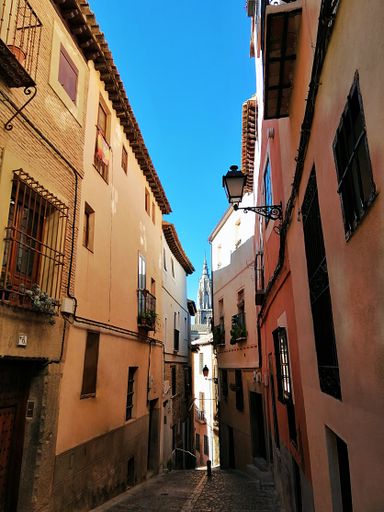 A vertical shot of a narrow street with colorful short buildings in Toledo, Spain
