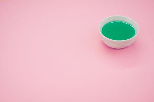 A white container with green liquid paint on a pink surface - copy space
