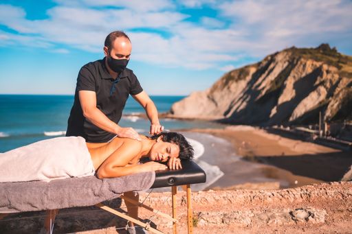 A closeup shot of a masseur in a facial mask doing massage to a Hispanic female on a seaside