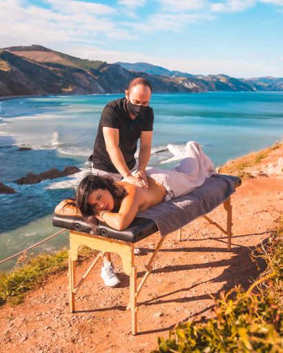 A vertical shot of a masseur in a facial mask doing massage to a Hispanic female on a seaside