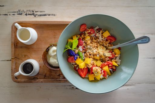 A top view of a bowl of porridge mixed with fruits served with yogurt and natural honey on a wooden tray