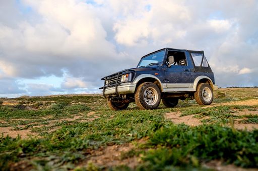 A blue car on the hill covered in the grass under the sunlight and a cloudy sky