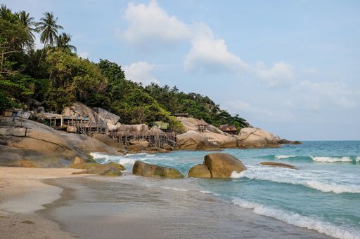 A beach surrounded by the sea and rocks covered in greenery under the sunlight
