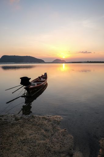 A boat on the sea surrounded by rocks with the sun reflecting on the water during the sunset