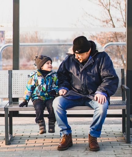 Young child and older man laughing while sitting in a bus stop