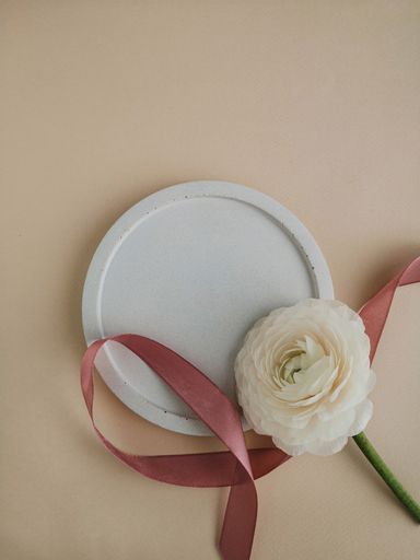 A top view of rose, ribbon, and a white plate isolated on pink background with copy space