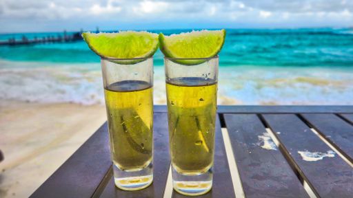 A closeup of two glasses of Tequila topped with freshly sliced limes on a wooden table in Mexico