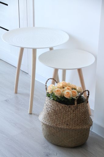 A vertical shot of a basket with roses next to small white tables indoors