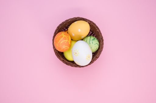 A top view of a basket of colored Easter eggs with various ornaments in the pink background