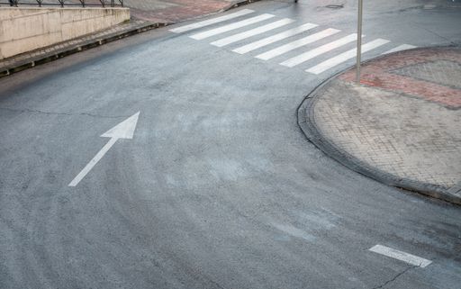 A high angle shot of a road curve with a white directional arrow and pedestrian crossing