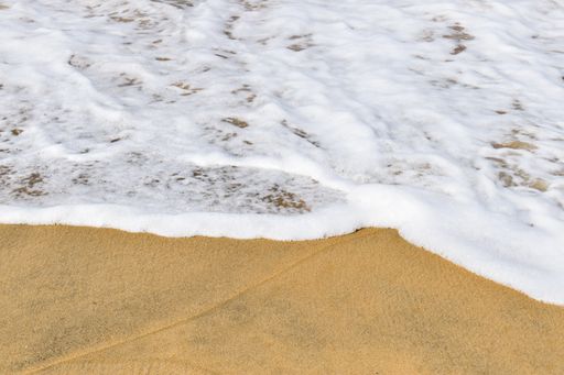 A closeup shot of white foamy waves and brown sand on the beach