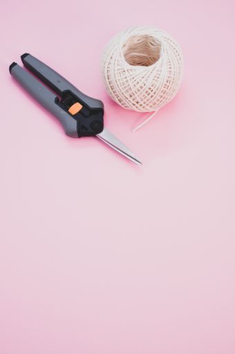 A vertical shot of a secateurs and yarn on a pink background with space for text