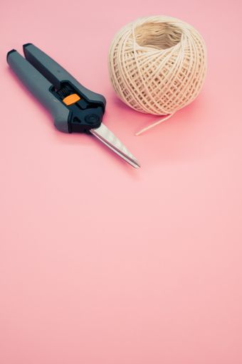 A vertical shot of a secateurs and knitting yarn on a pink background with space for text