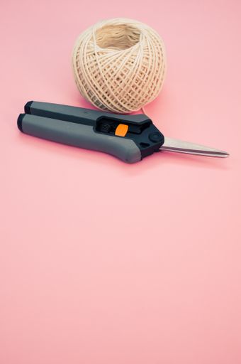 A high angle view of secateurs and knitting yarn isolated in the pink background with copy space