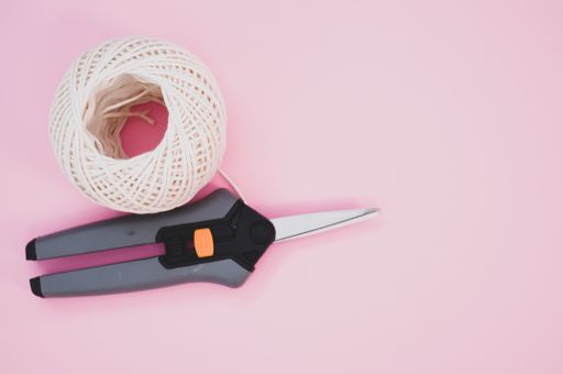 A secateurs and knitting yarn on a pink background with space for text