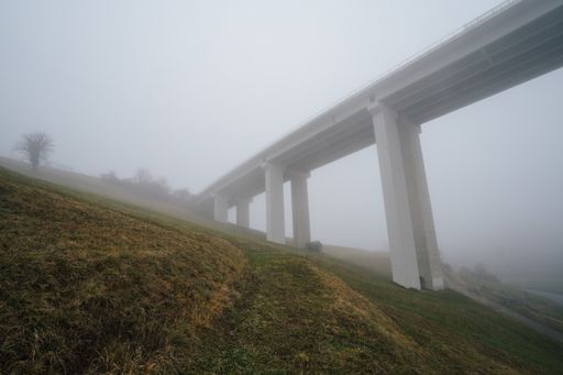 A concrete bridge on a hill surrounded by greenery covered in the fog under a cloudy sky