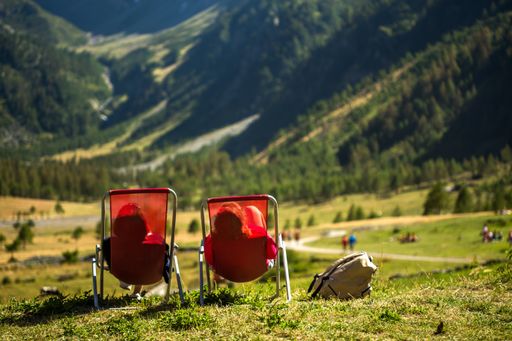 A grassy field with two people laying on chairs enjoying the view