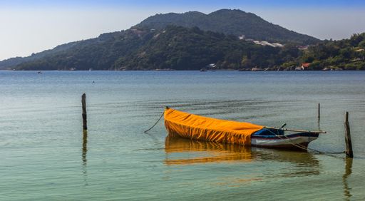 A canoe tied on the wood in the lake surrounded by the mountains against the blue sky